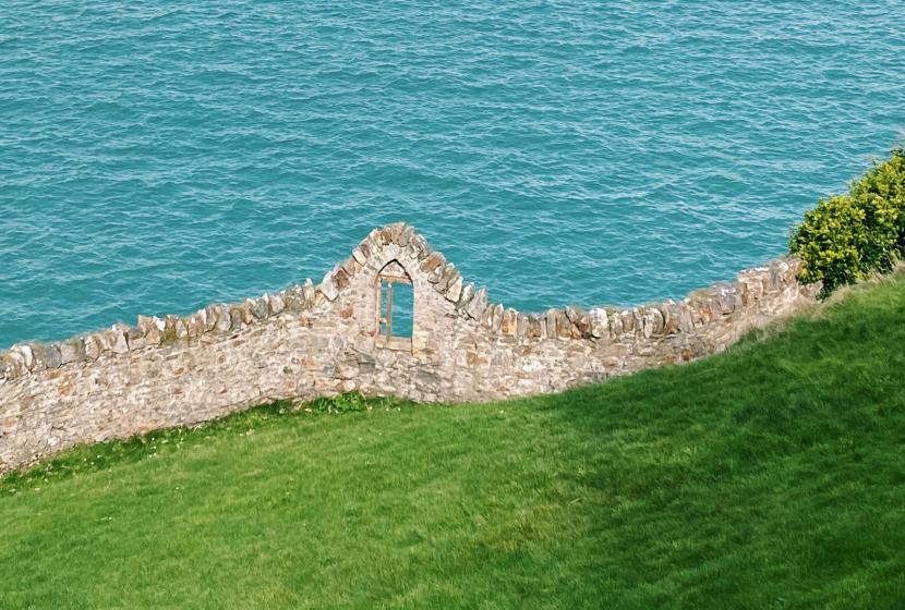 A stone wall along a green hill overlooking the ocean with an island in the distance