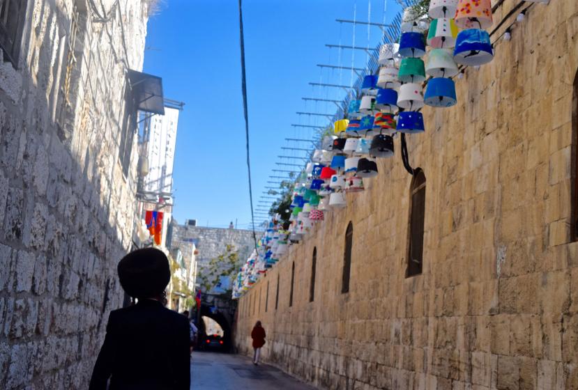 A man walks along a walled street in Jerusalem with colorful lanterns 