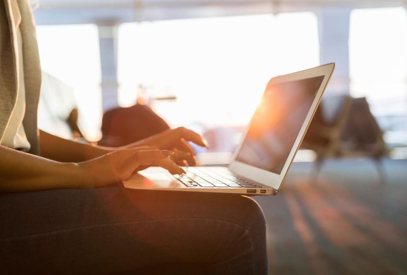 Closeup of a woman's hands typing on a laptop as she sits in an airport